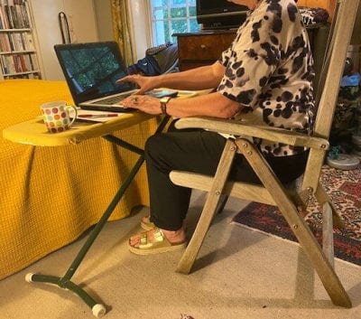 Home office - woman sat in garden chair with laptop on ironing board